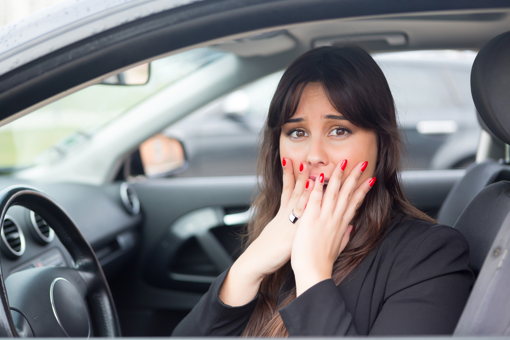 Woman sitting in car holding both hands on her face in shock