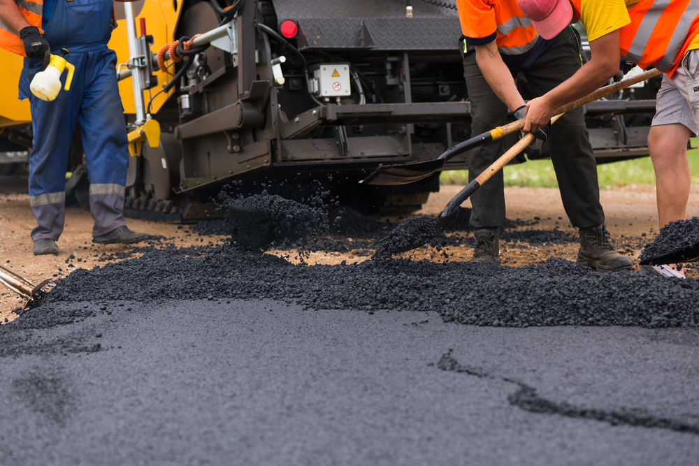 road workers levelling out asphalt with a machien in the background