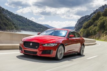 red Jaguar XE on the road going round a corner with mountains in the background