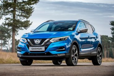 Metallic blue nissan qashqai parked on tarmac with trees in the background