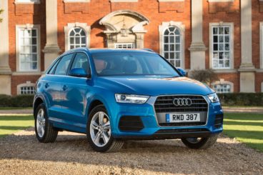 bright blue Audi Q3 parked on pavement with country house in the background
