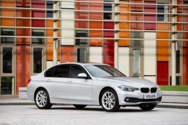 BMW 3 Series Saloon in silver parked with a multi colour windowed building behind