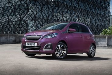 a dark purple peugeot 108 hatch parked on tarmac with modern in the background