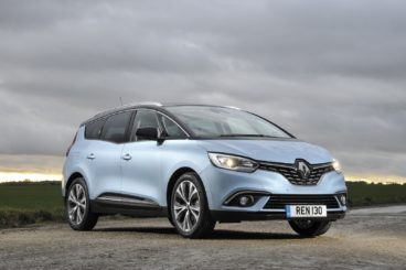 metallic blue renault grand scenic parked on gravel at sunset with green grass in the background