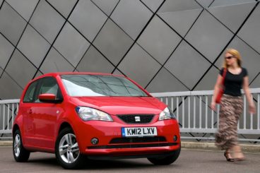 a bright red seat mii hatchback parked in city with women walking by