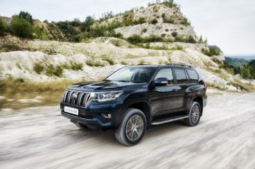 a dark coloured toyota land crusier driving on white road with cliffs in the background