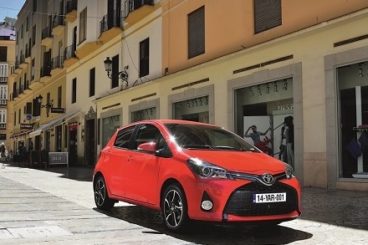 Red Toyota Yaris driving along city streets with the sun shining
