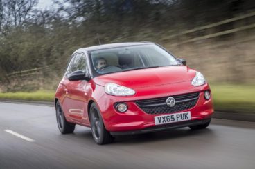 a bright red vauxhall adam driving on tarmac road with blurred trees in the background