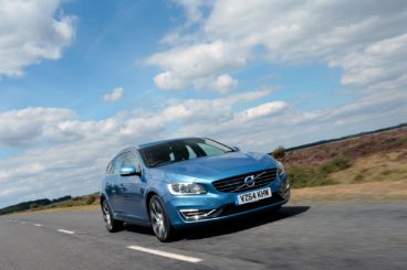 a metallic blue volvo v60 sportswagen driving down tarmac road with grass on either side