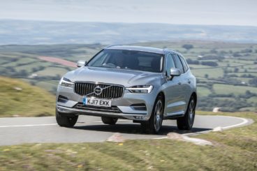 a metallic coloured volvo xc60 estate driving on tarmac road with green hills in the background