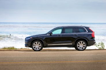 a dark coloured Volvo xc90 estate parked on tarmac road with the sea in the background