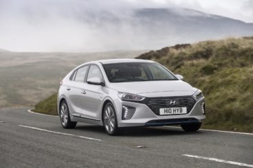 a metallic hyundai ioniq hatchback driving on tarmac road with mistly hills in the background
