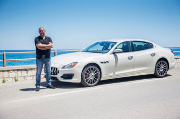 Guy standing with arms crossed next to a white Maserati Quattroporte