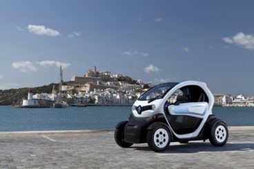 a white and blue renault twizy coupe parked of grey brick road with europeon island in the background