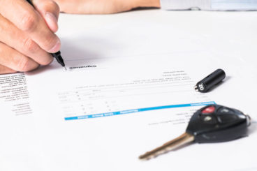 Man signing documents with keys placed on top