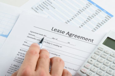 person looking over lease agreement with a pen and calculator next to them