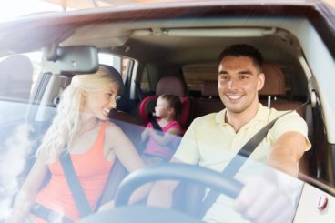 two adults and a young child in a car seat sitting in the car smiling