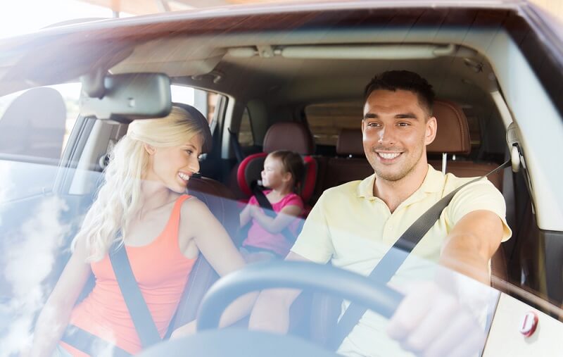two adults and a young child in a car seat sitting in the car smiling