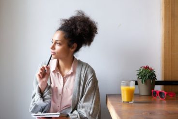Woman starring in to the distance with pen resting on chin