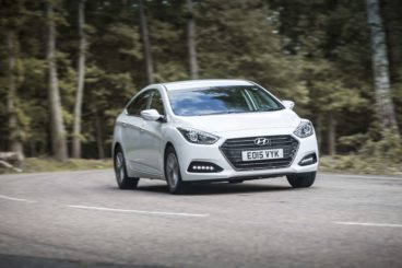 Hyundai i40 in white driving along a country road with trees in the background