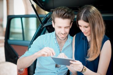 young couple sitting in the boot of a car looking on an iPad