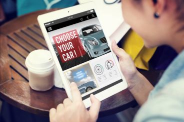 person sitting at a wooden table with a takeaway coffee looking at car deals on an ipad