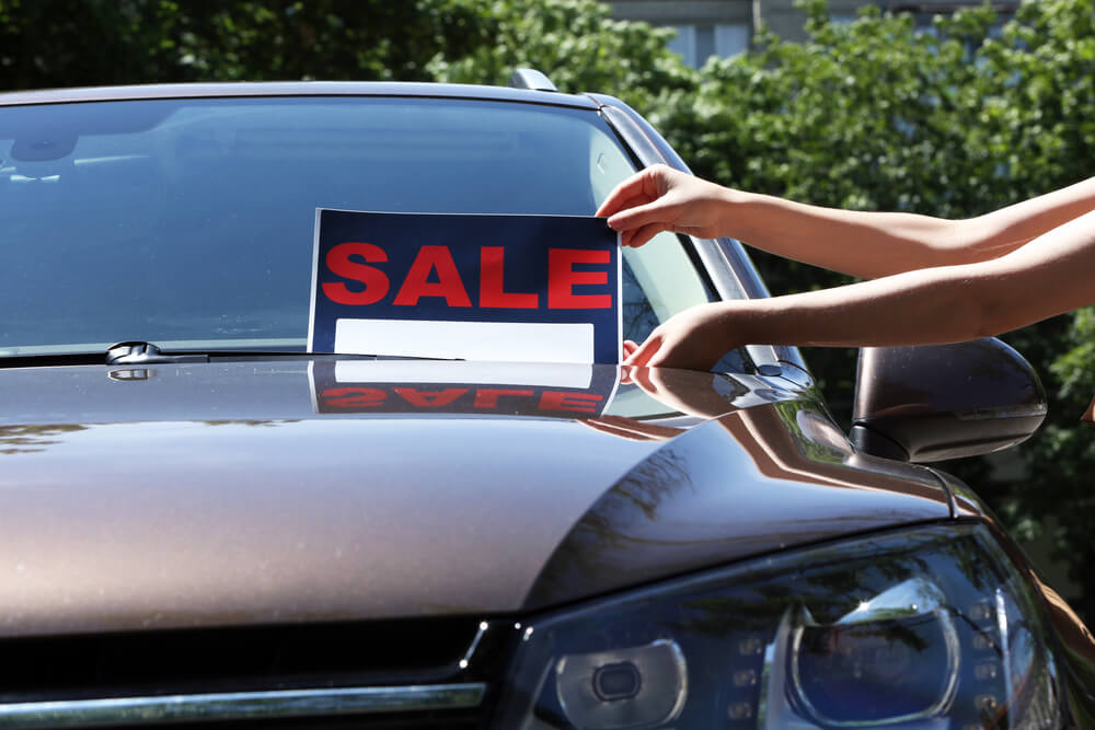 person putting a sale sign on a second hand car