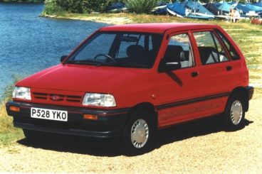 A red kia pride parked beside a lake
