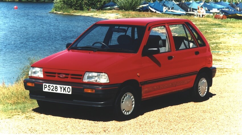 A red kia pride parked beside a lake