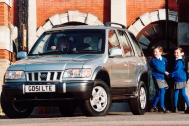 a Kia Sportage parked with two school children playing behind