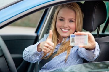 girl in car, holding out driving licence with a thumbs up - First Car