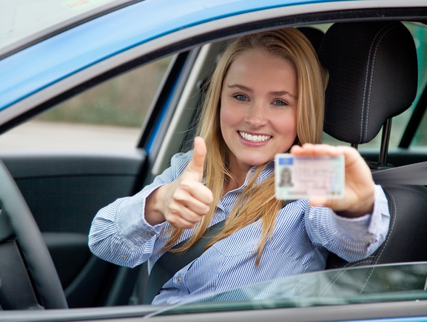 girl in car, holding out driving licence with a thumbs up - First Car