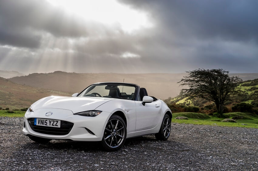 Mazda MX-5 in white parked on a country road with the sun shining through the clouds