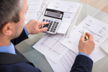 businessman in a suit doing calculations on a calculator with paperwork