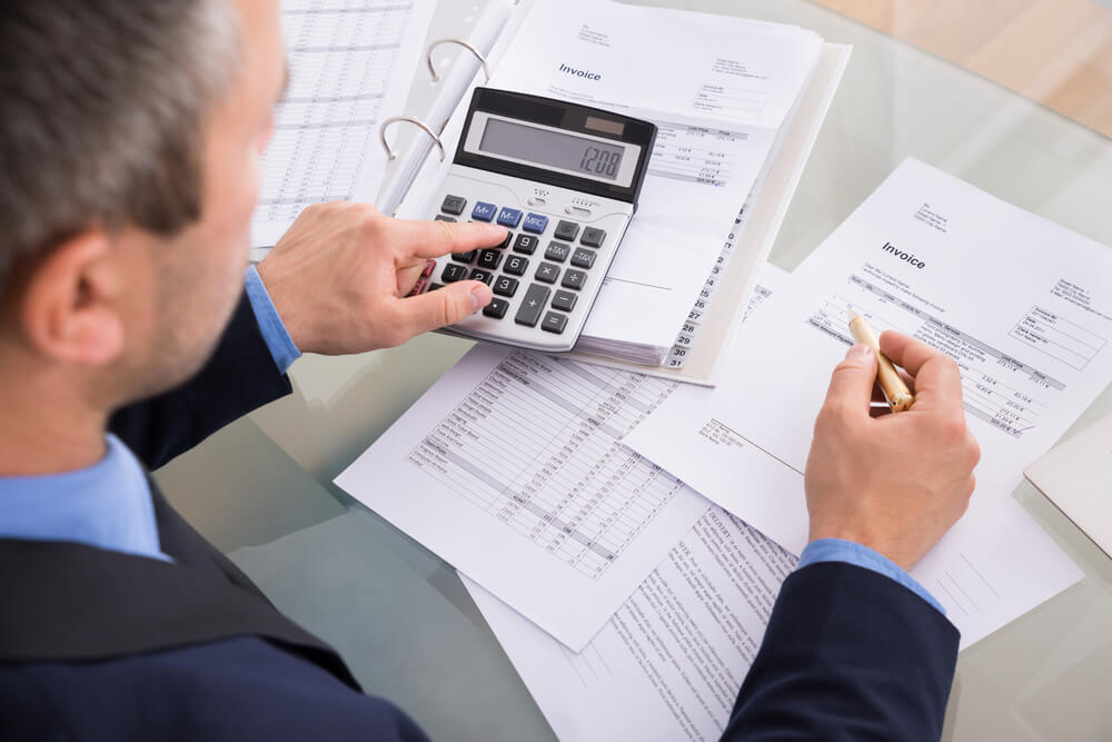 businessman in a suit doing calculations on a calculator with paperwork