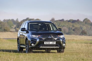 Mitsubishi Outlander Phev in black parked on a green field with trees in the background