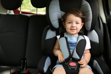 toddler with brown hair sitting in a car seat in a car smiling