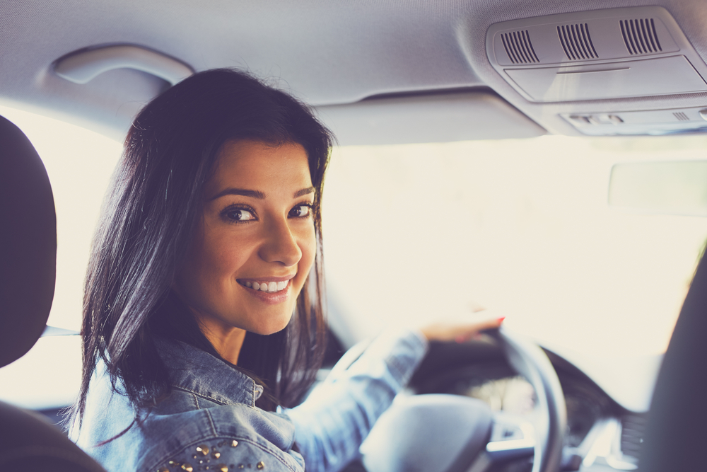 Lady looking back from the steering wheel smiling - First Car