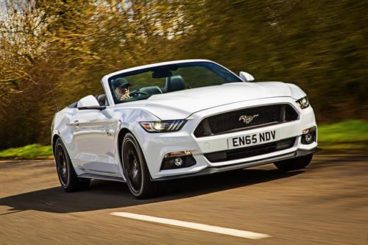white ford mustang driving on tarmac road with trees in the background