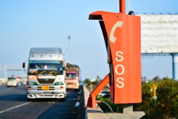 picture of an orange SOS telephone on the side of a motorway with a lorry coming towards it