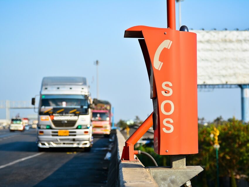 picture of an orange SOS telephone on the side of a motorway with a lorry coming towards it