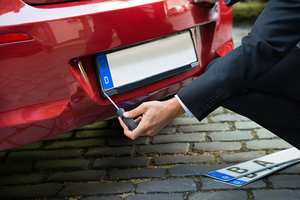 man in a suit replacing a registration plate on a red car