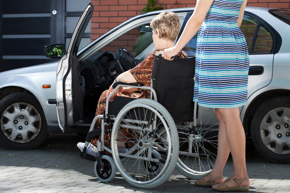 woman pushing a wheelchair next to a silver car