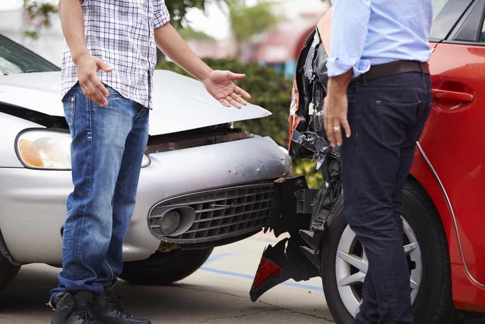 a silver car crashing into the back of a red car with two men in shirts and trousers at the scene