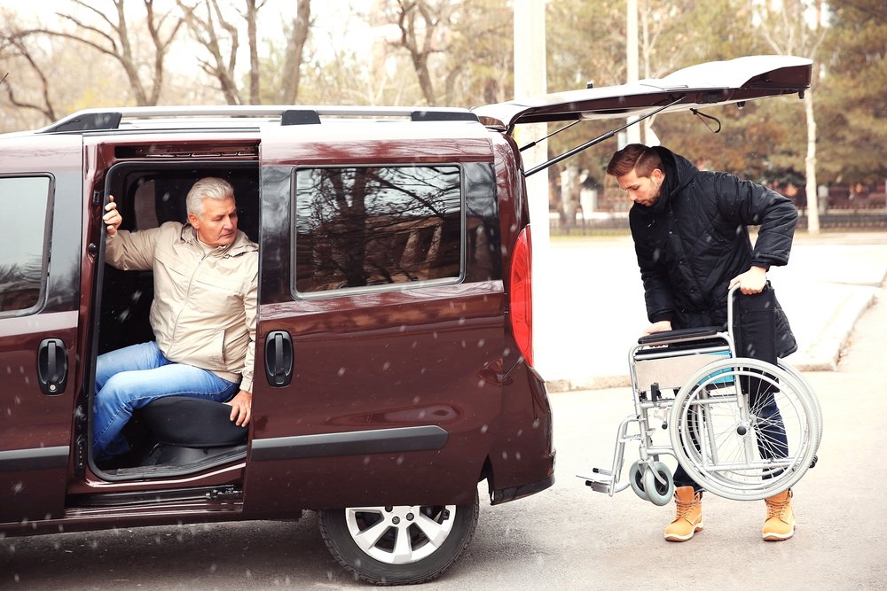 man putting wheelchair in a brown car with an older man sitting in the car