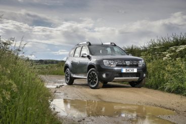 Black Dacia Duster off road on a muddy track surrounded by grass and a muddy puddle