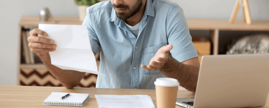 Man at desk looking confused at paper and laptop