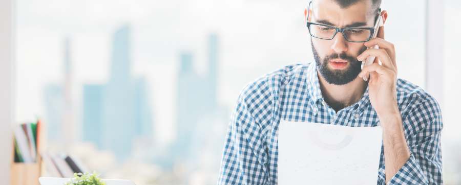 Man on phone looking at paperwork, not happy