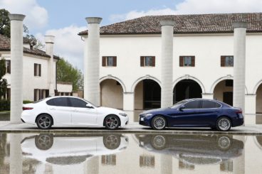 Two alfa romeo guilia saloons parked outside white building with their reflections in the big puddles in front