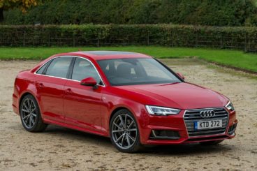 red Audi A4 parked on gravel with grass and trees in the background